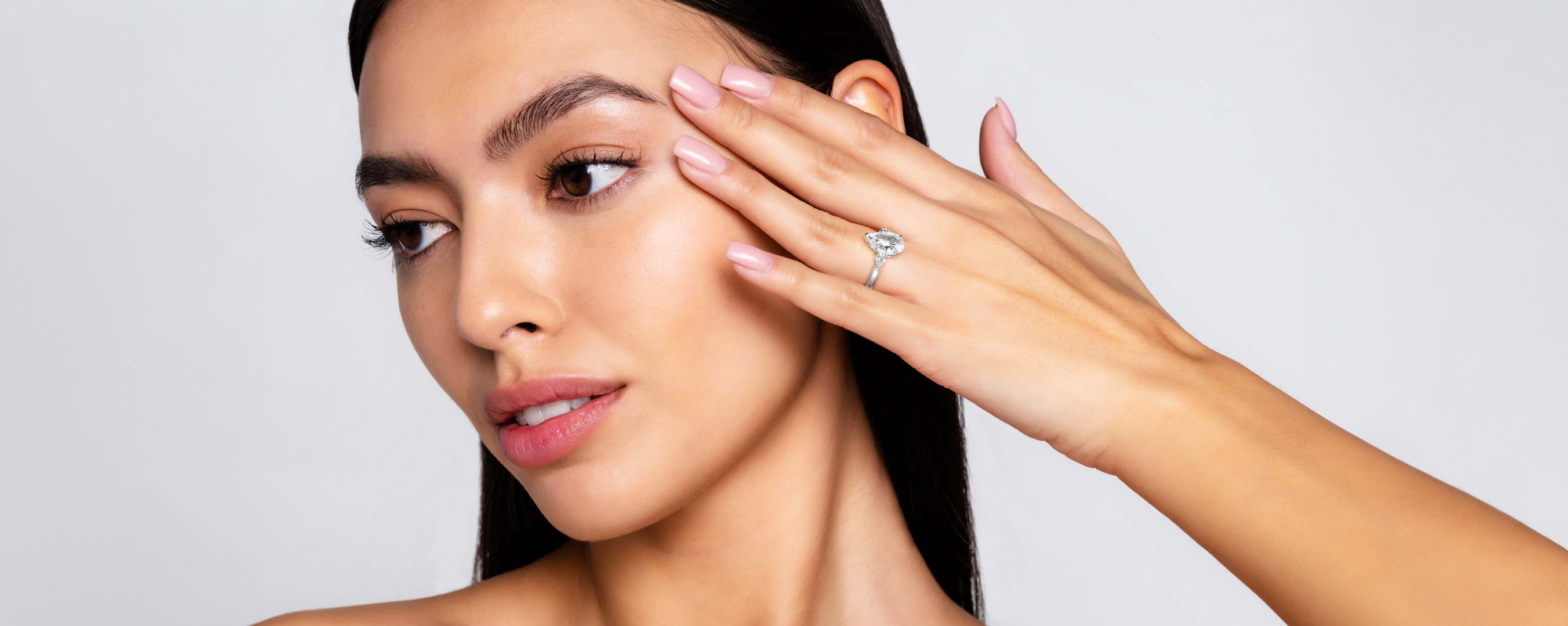 Portrait of a woman displaying a pear-cut diamond engagement ring with two smaller pear-cut diamonds on either side of the centre stone. The platinum band enhances the brilliance of the trio of diamonds, creating a balanced and elegant design. Her manicured nails and flawless complexion highlight the ring’s sparkle, making it the focal point of the image. Ideal for showcasing the beauty of a pear-cut engagement ring with a modern and sophisticated style.